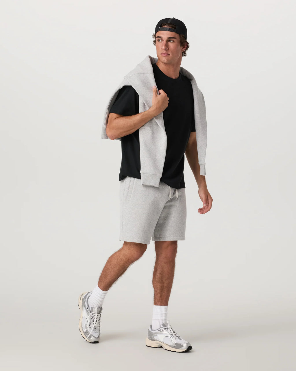 Person wearing a black t-shirt, gray shorts, and white sneakers on a light gray background