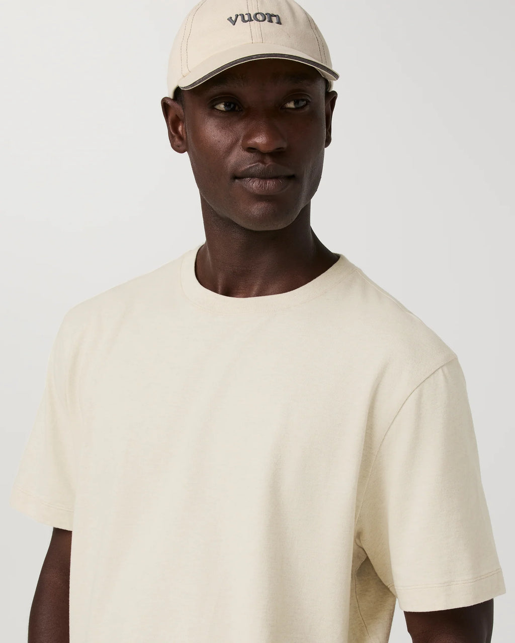 A man wearing a cream-colored crewneck t-shirt and a matching cream-colored Vuon baseball cap, photographed against a plain light gray background.