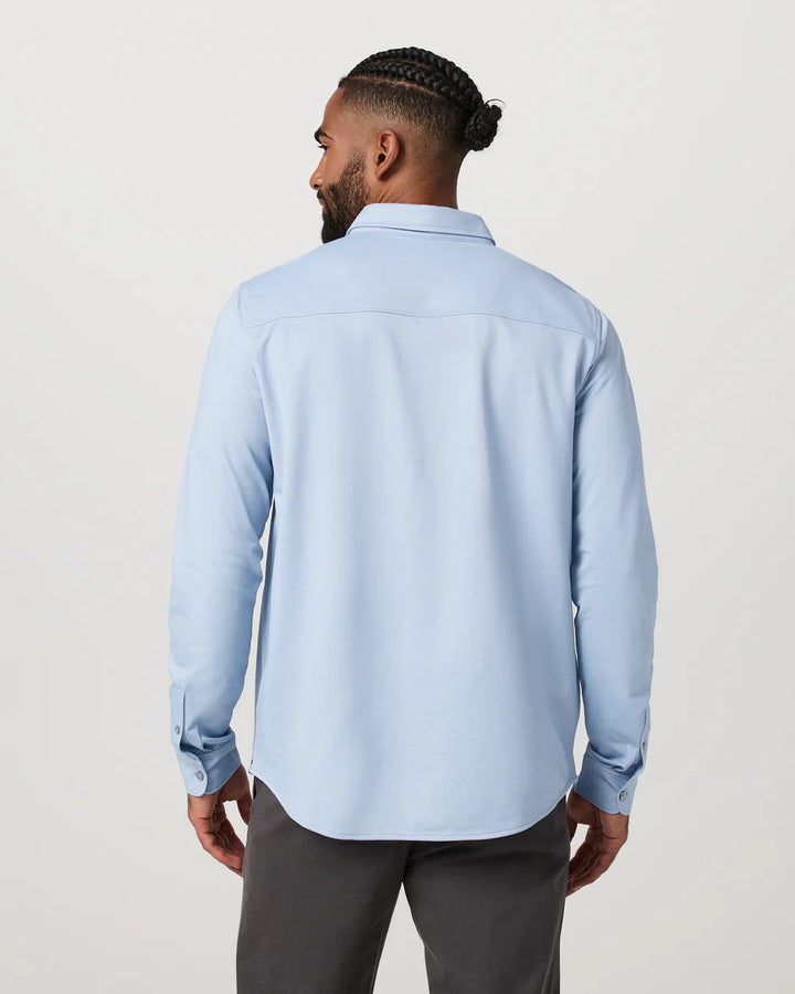 Man wearing a light blue shirt and dark pants on a plain background