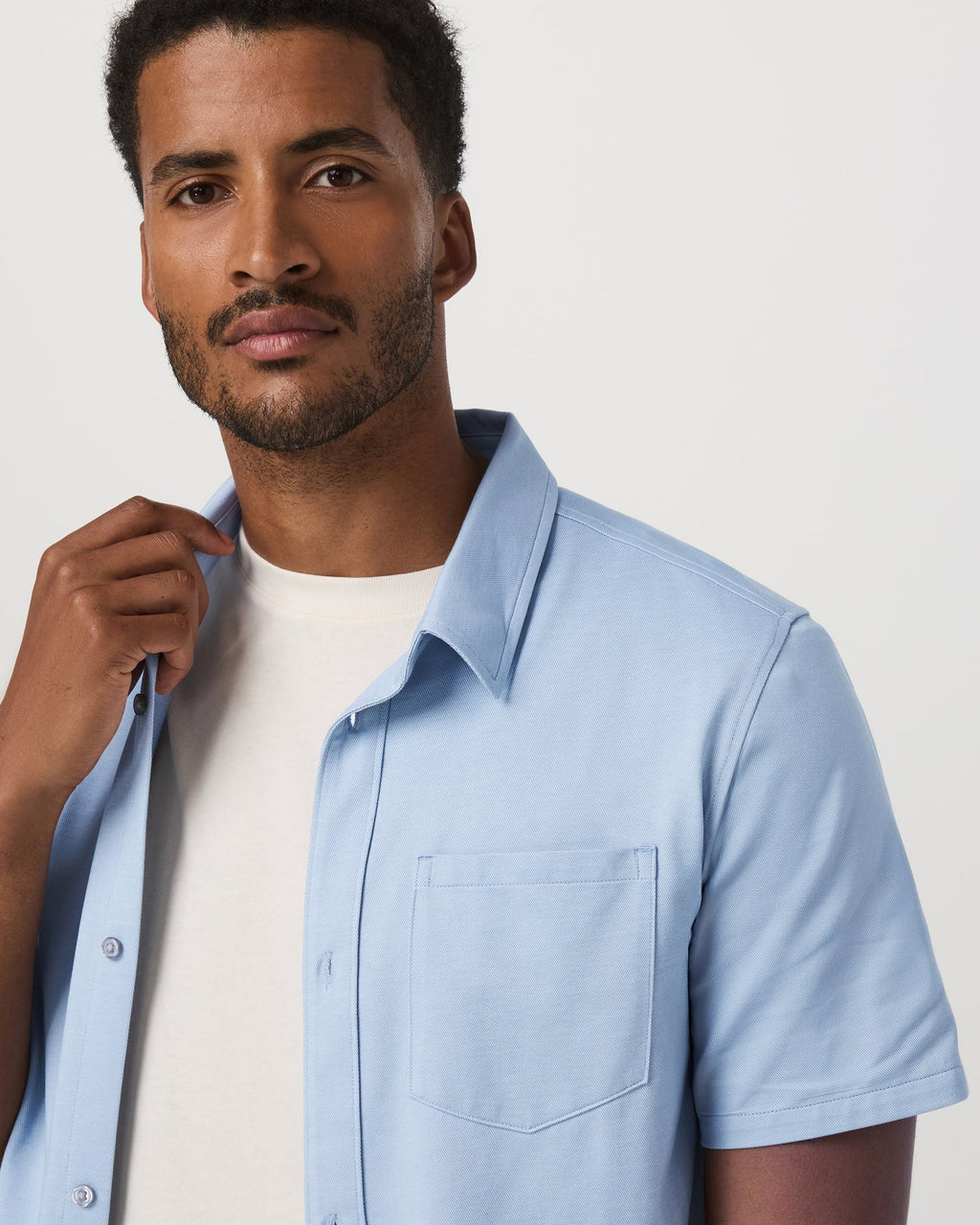 Man wearing a light blue shirt over a white t-shirt against a plain background