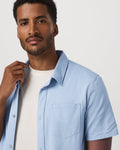 Man wearing a light blue shirt over a white t-shirt against a plain background