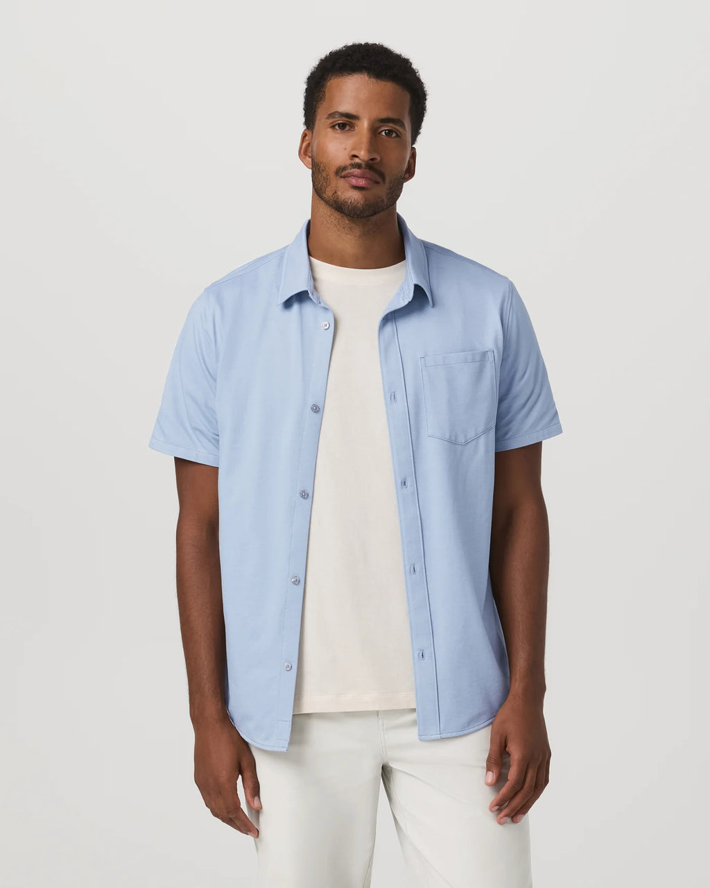Man wearing a light blue short-sleeve shirt over a white t-shirt on a plain background