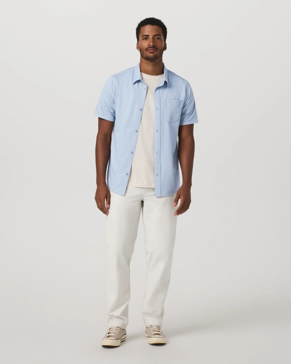 Man wearing a light blue shirt and white pants on a plain background