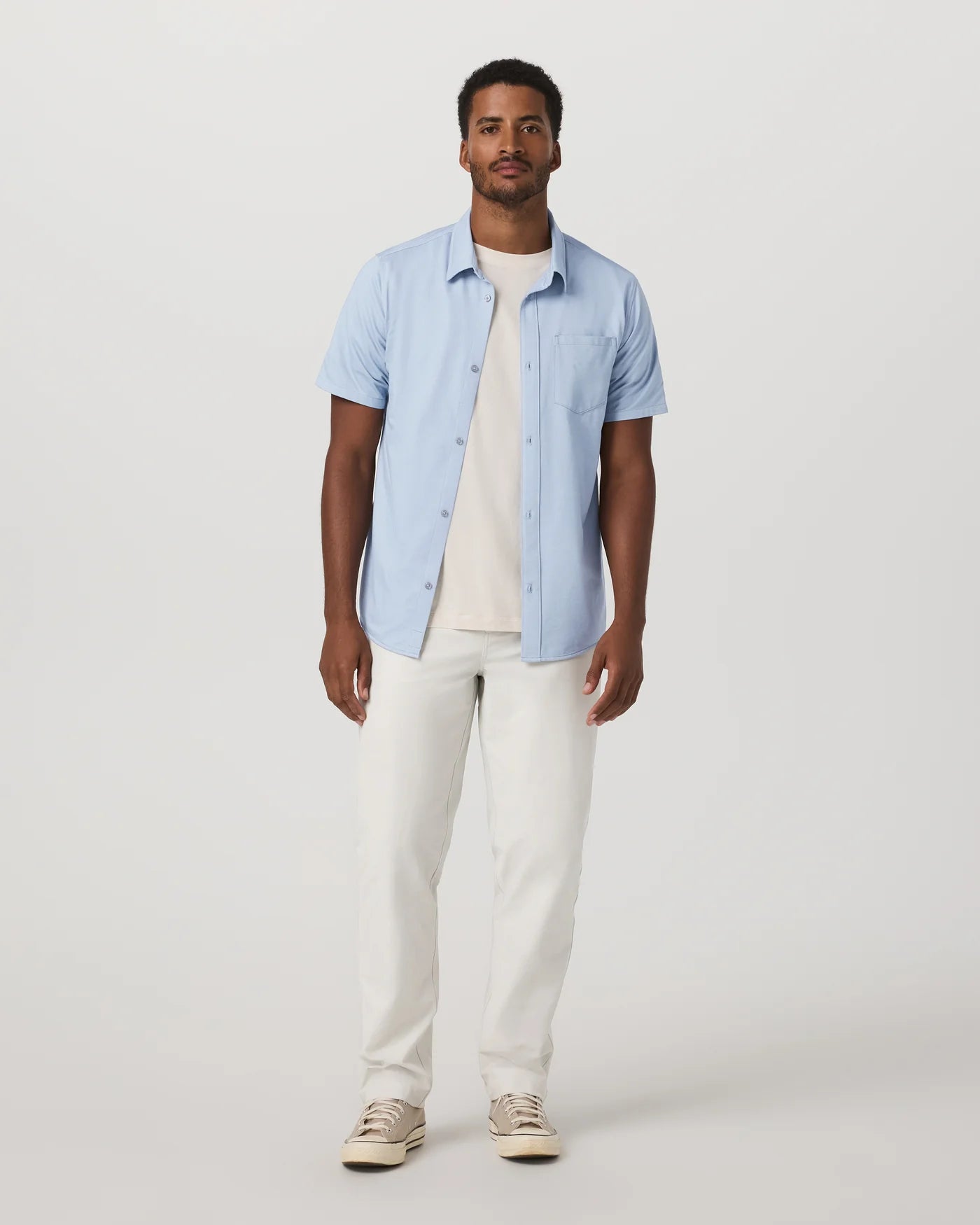 Man wearing a light blue shirt and white pants on a plain background
