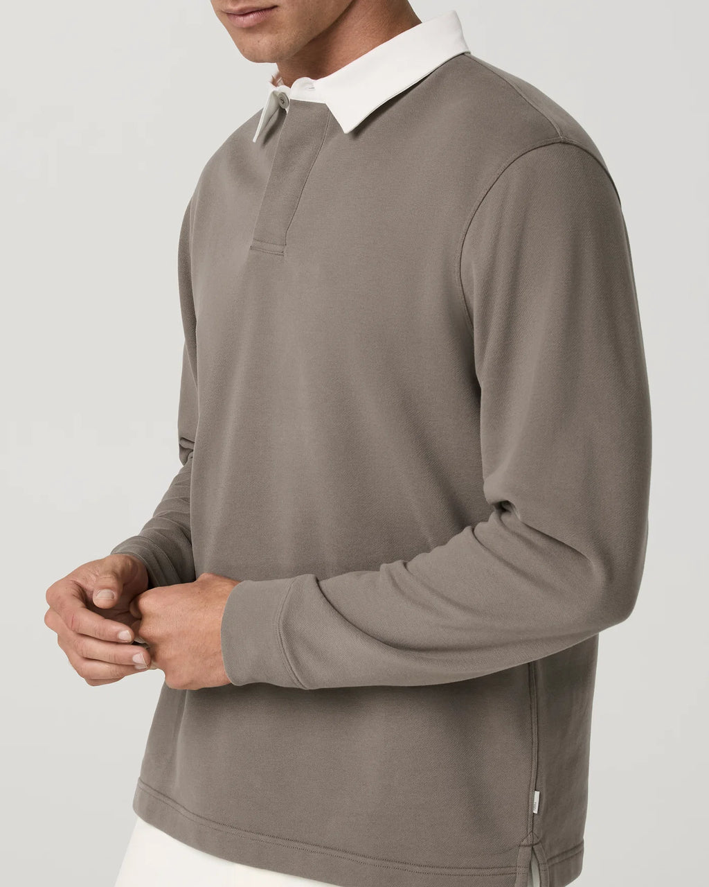 A man wearing a taupe-brown long-sleeve rugby shirt with a white collar, shown from the chest down against a light gray background.