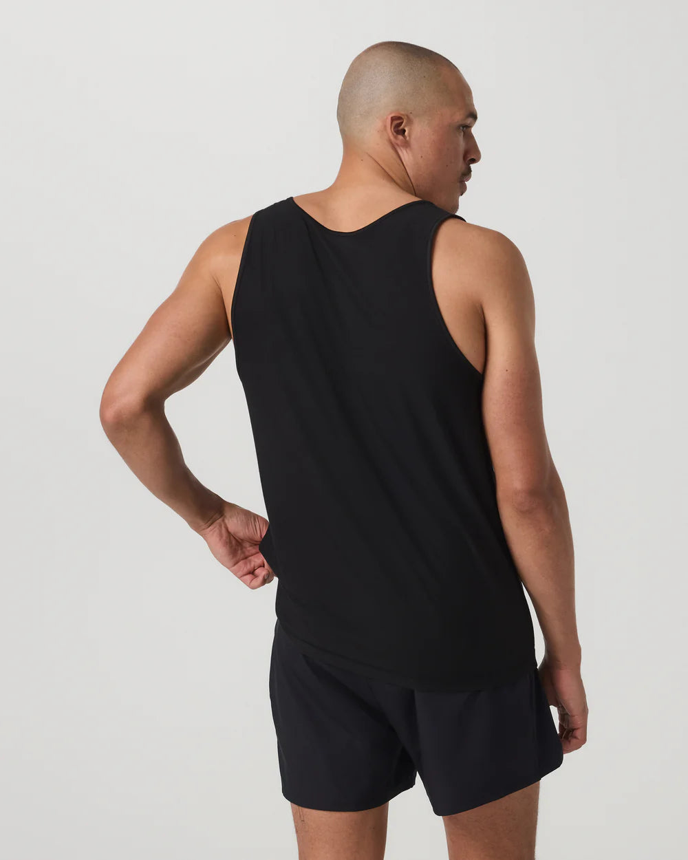 Man wearing a black tank top and shorts on a light gray background