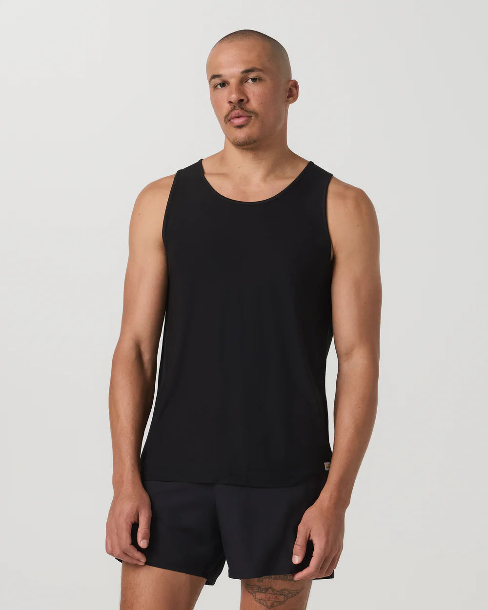 Man wearing a black tank top and shorts on a plain background