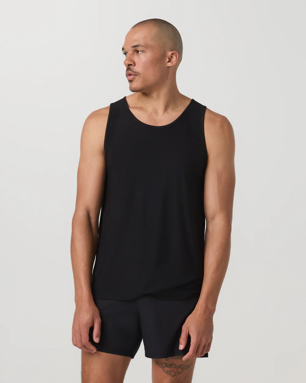 Man wearing a black tank top and shorts on a plain background