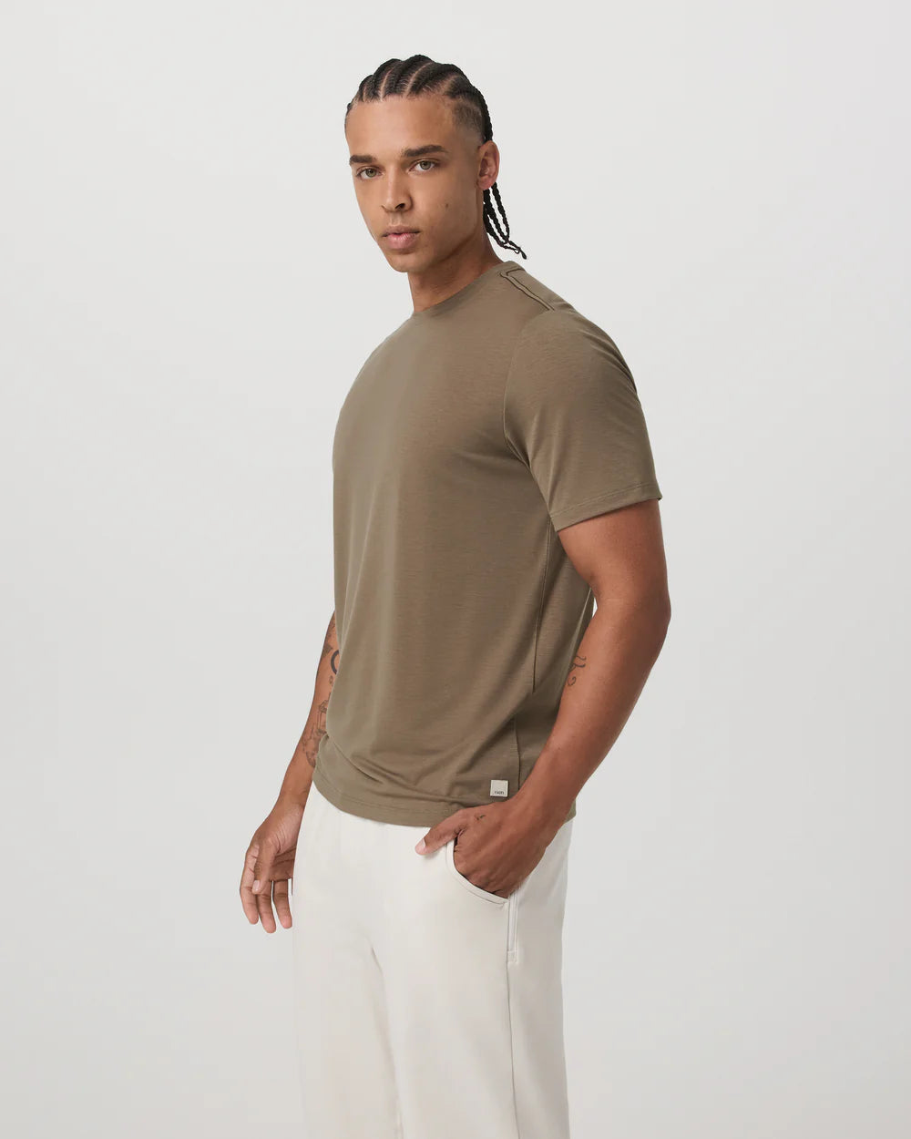 Man wearing a brown t-shirt and white pants on a light gray background