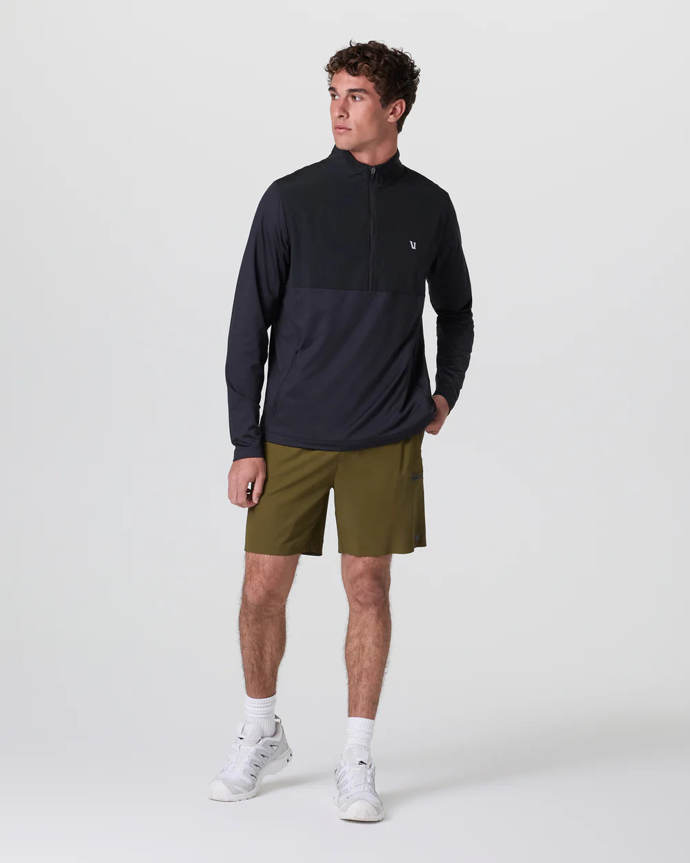 Man wearing a black long-sleeve athletic shirt and green shorts on a white background