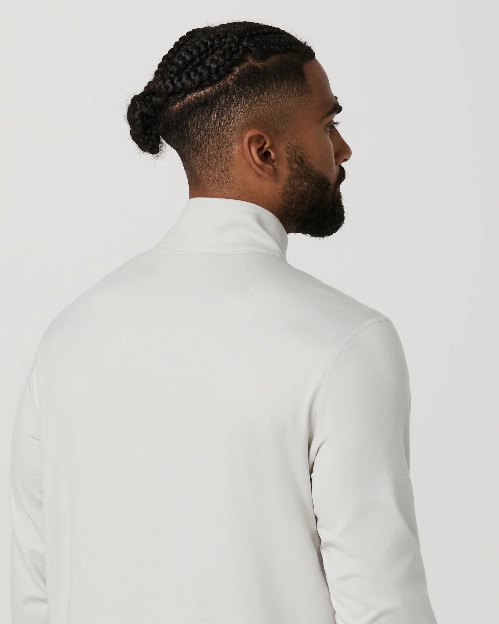 A man shown from the back wearing a white mock neck long-sleeve shirt against a light gray studio background.