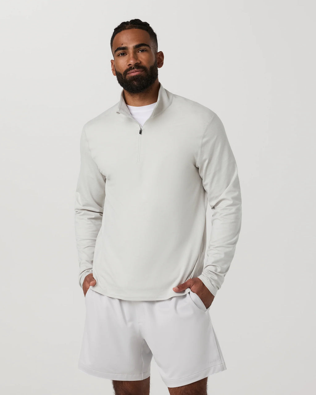 A man wearing a light gray quarter-zip long-sleeve shirt and matching light gray shorts, standing against a plain light gray studio background.