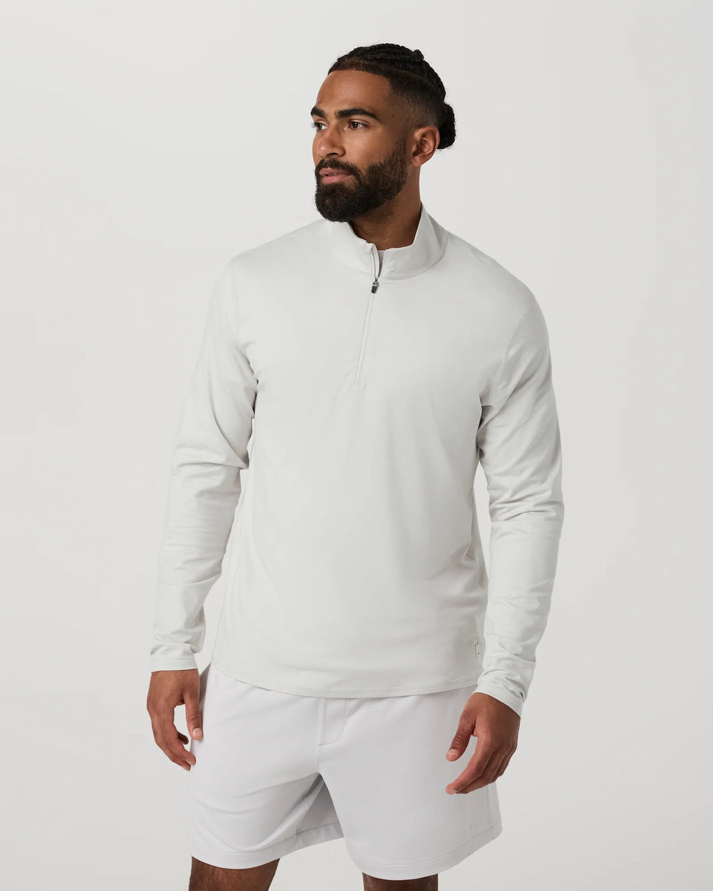 Man wearing a light gray long-sleeve athletic shirt and white shorts on a plain background