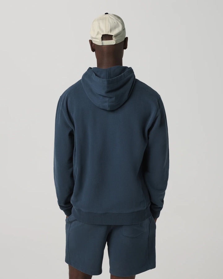 Person wearing a navy blue hoodie and shorts set with a beige cap on a light gray background