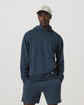 Man wearing a navy hoodie and shorts set with a cap on a light gray background