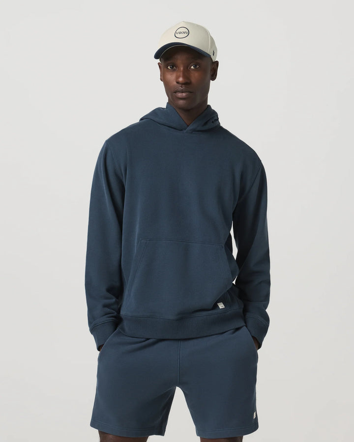 Man wearing a navy hoodie and shorts set with a cap on a light gray background