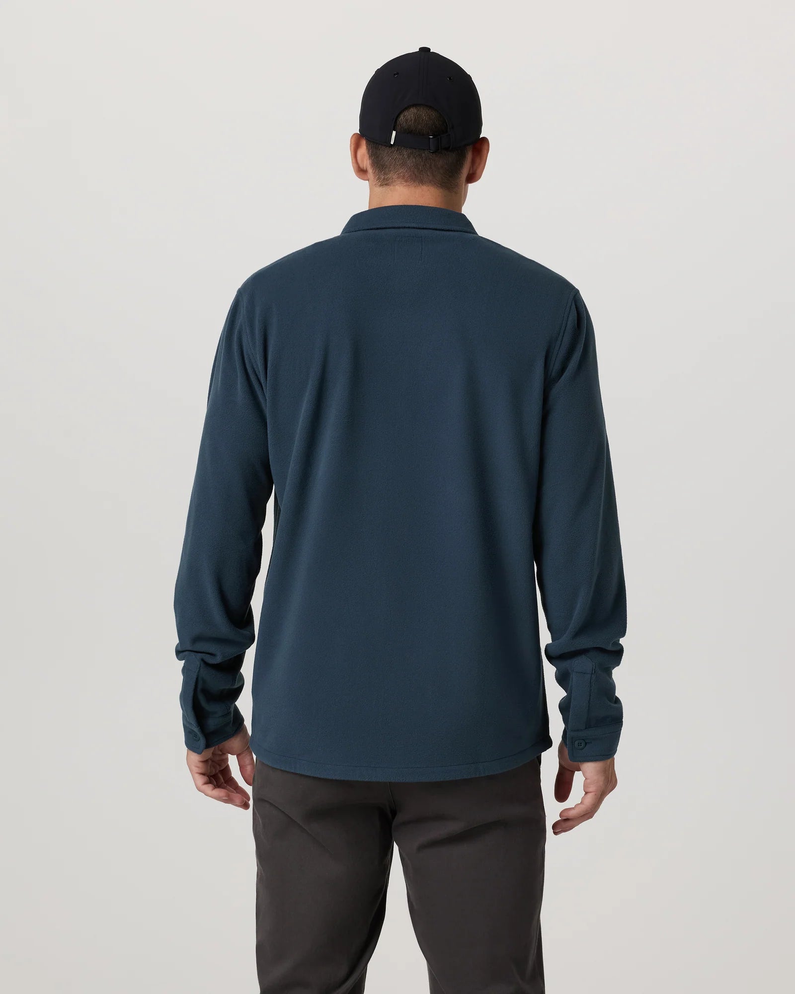 Person wearing a dark blue long-sleeve shirt and black cap on a light gray background