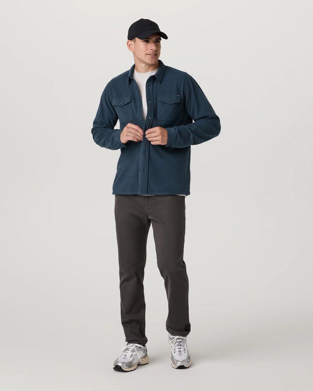 Man wearing a blue jacket, black pants, and a black cap on a white background
