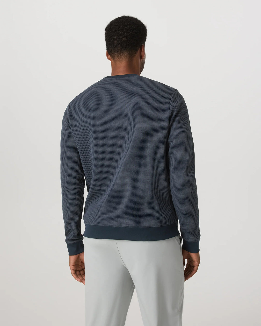 Man wearing a dark blue ribbed sweater and light gray pants on a white background