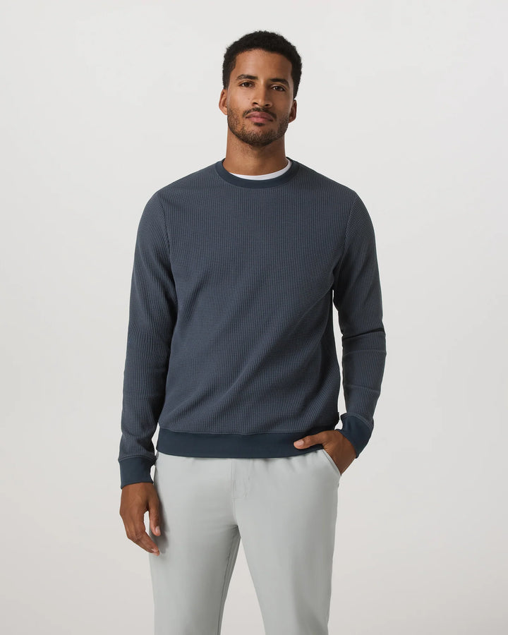Man wearing a dark blue ribbed sweater and light gray pants on a white background