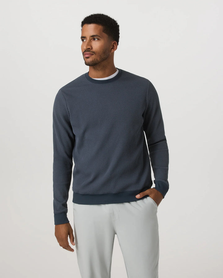 Man wearing a dark blue sweater and light gray pants on a white background