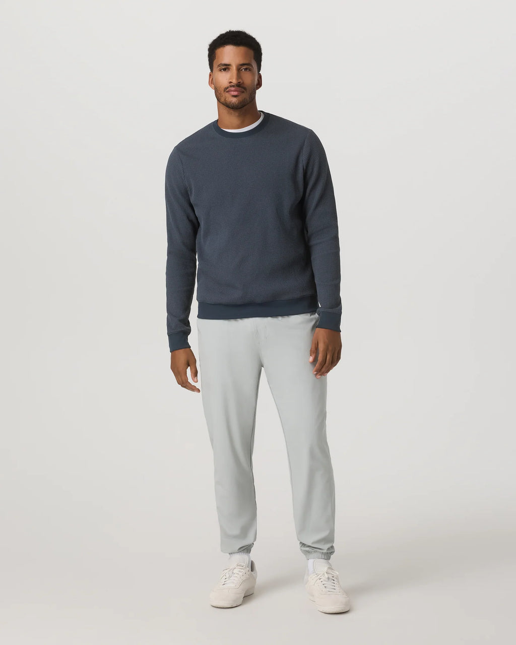 Man wearing a navy sweater and light gray pants on a white background