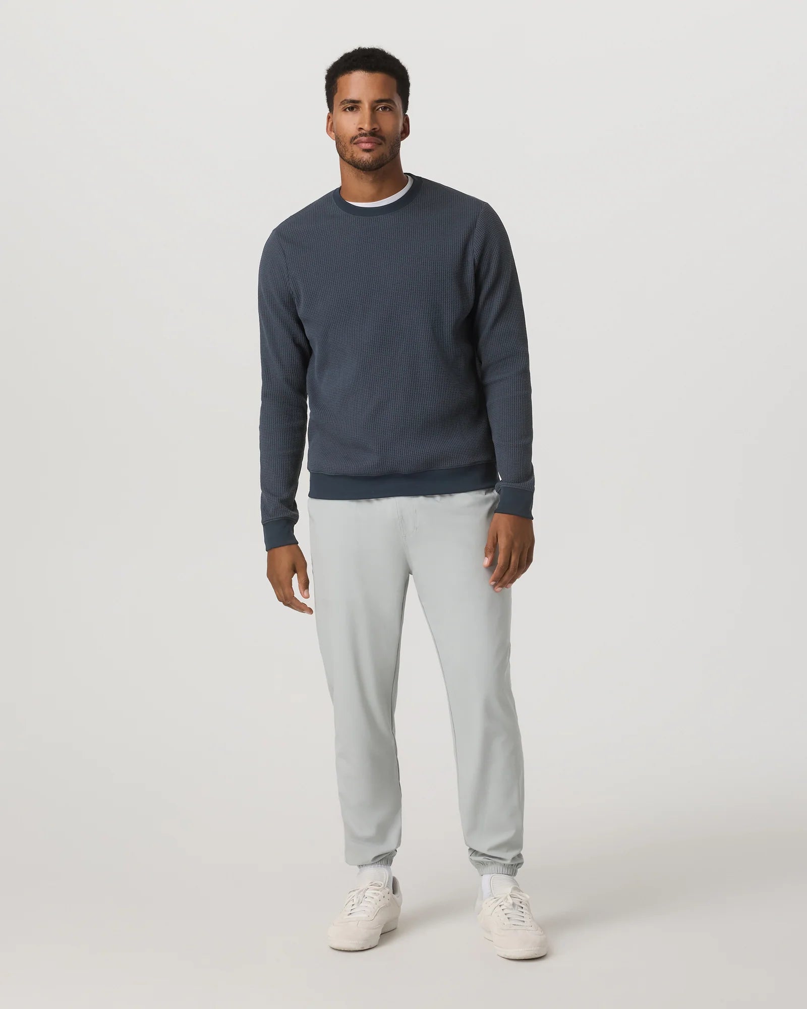 Man wearing a navy sweater and light gray pants on a white background