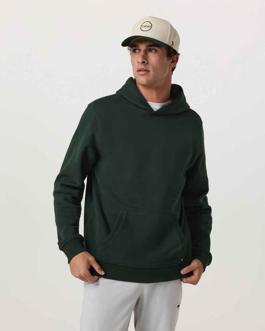 Man wearing a green hoodie and white pants on a plain background