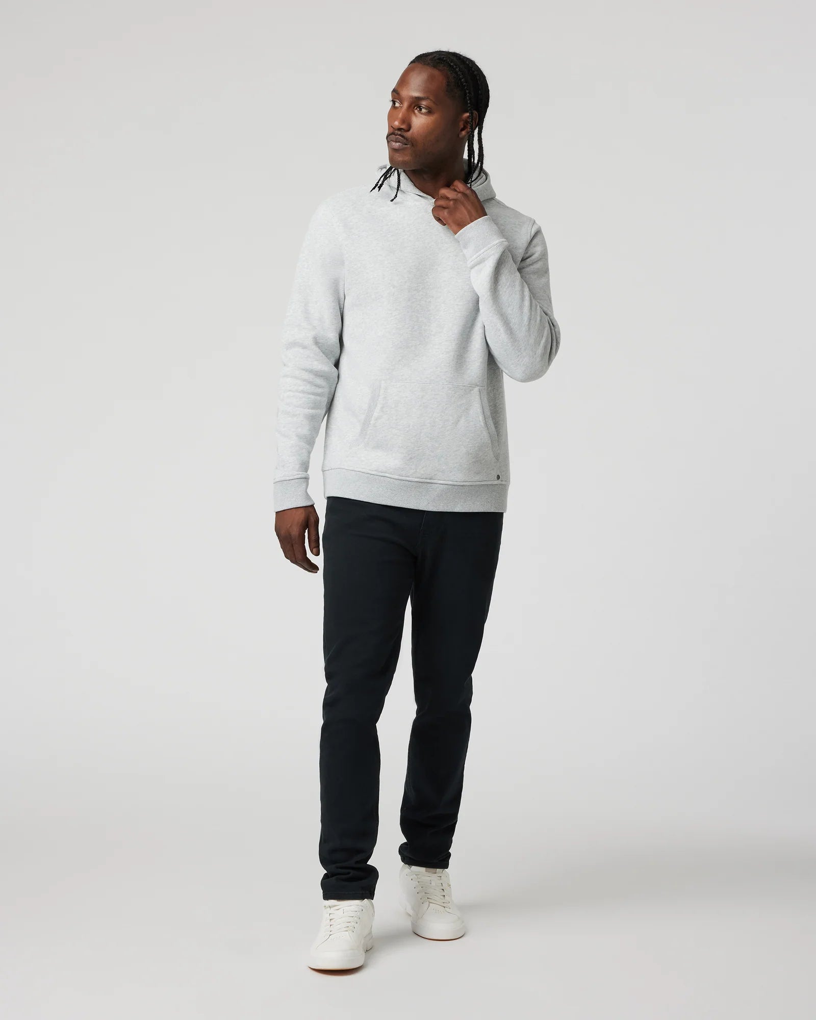 A man modeling a light gray crewneck sweatshirt, black slim-fit pants, and white sneakers against a plain light gray studio background.