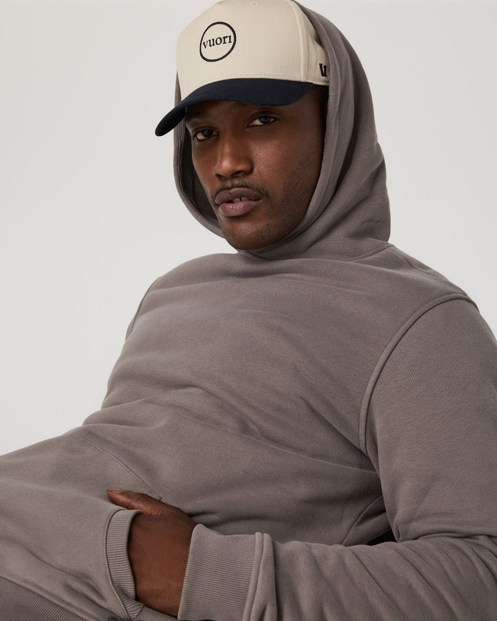 Person wearing a beige hoodie and cap with 'vuori' logo on a plain background
