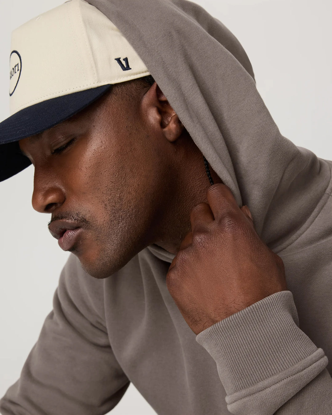 Man wearing a beige cap and gray hoodie against a white background