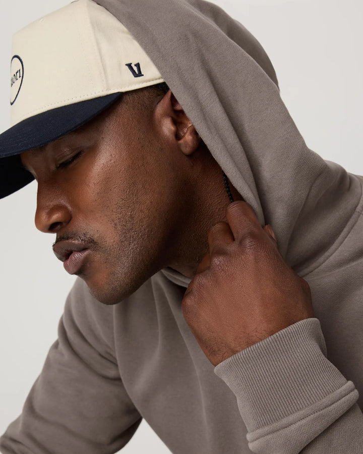 Man wearing a beige cap and gray hoodie against a white background