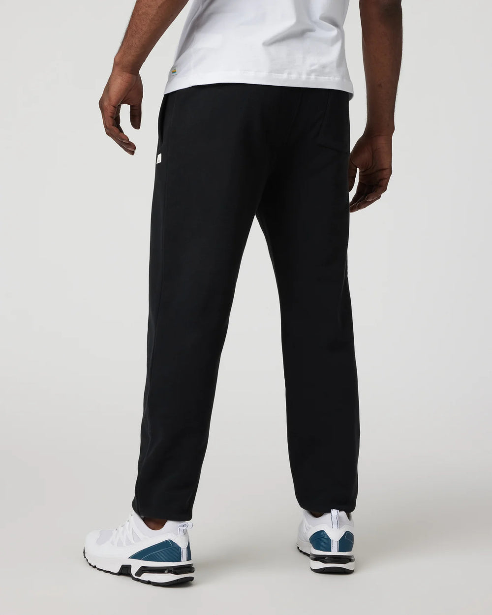 Person wearing black pants and white sneakers on a plain background