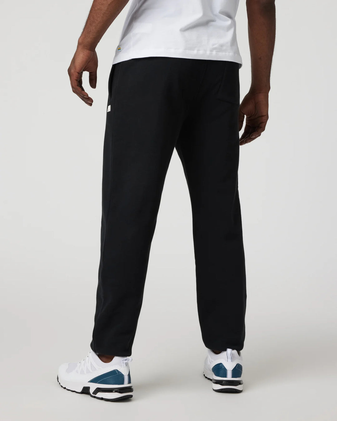 Person wearing black pants and white sneakers on a plain background