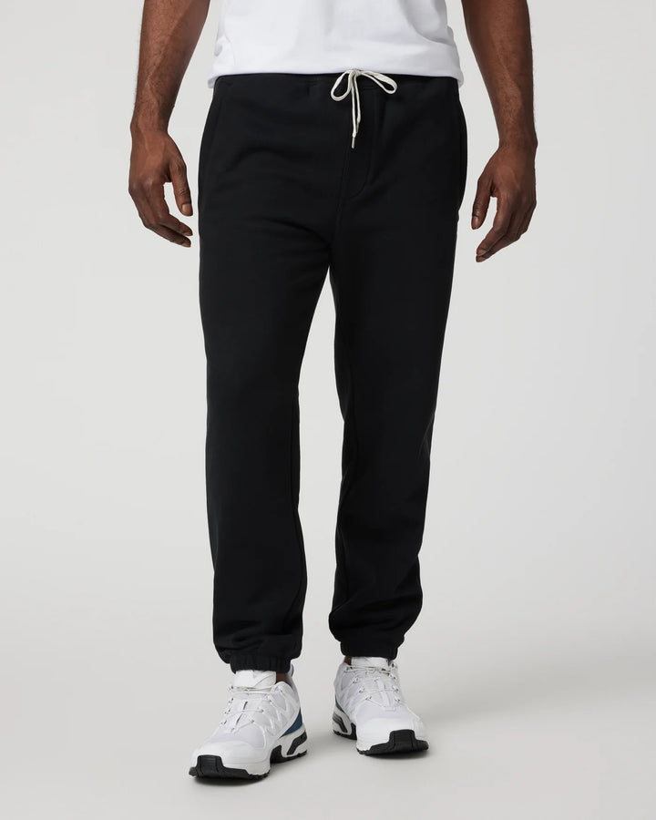 Person wearing black sweatpants and white sneakers on a plain background