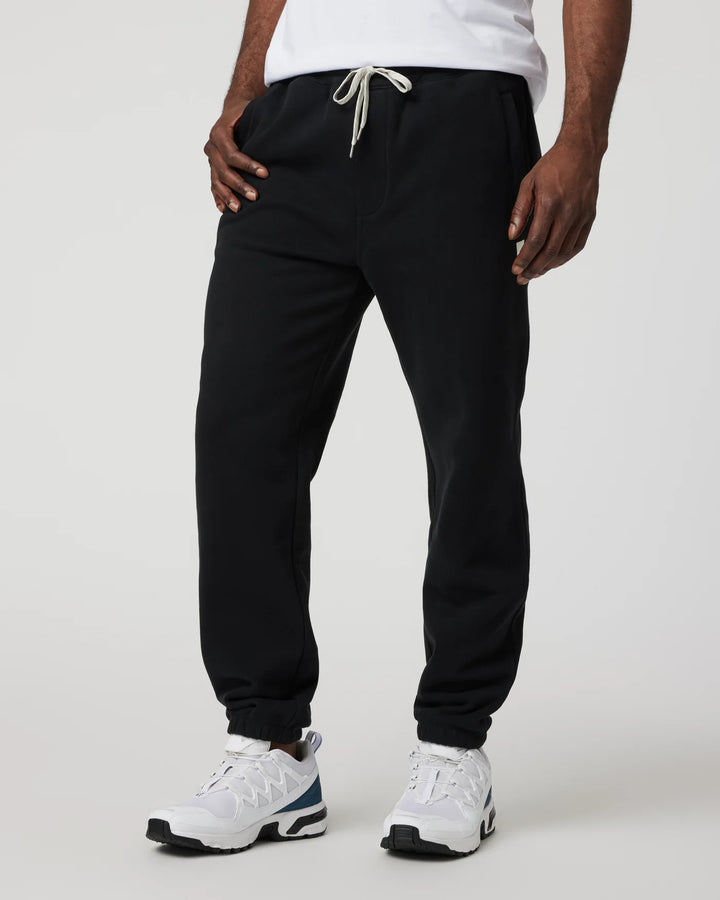 Person wearing black jogger pants and white sneakers on a plain background