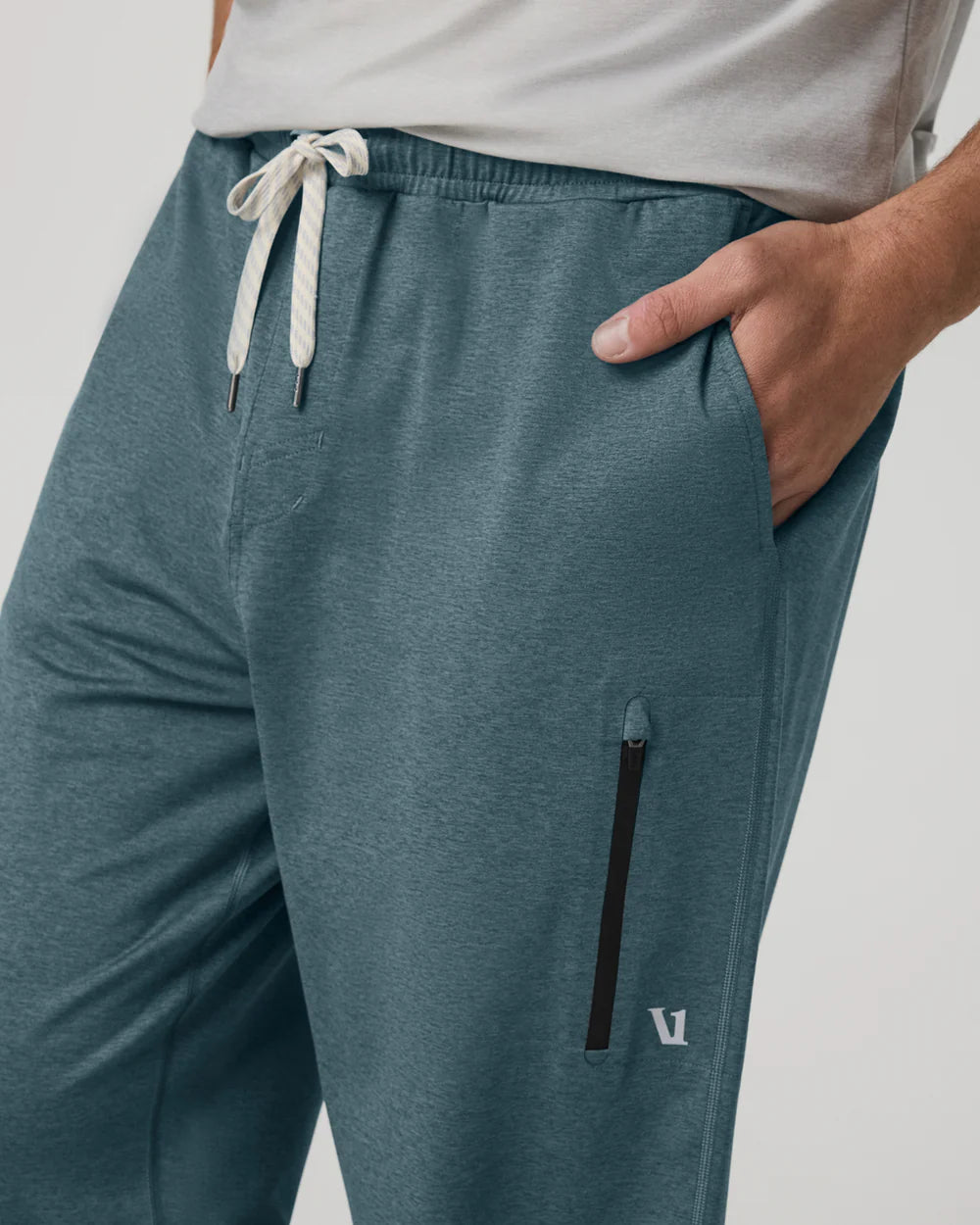 Teal jogger pants with a drawstring and zipper pocket on a light gray background