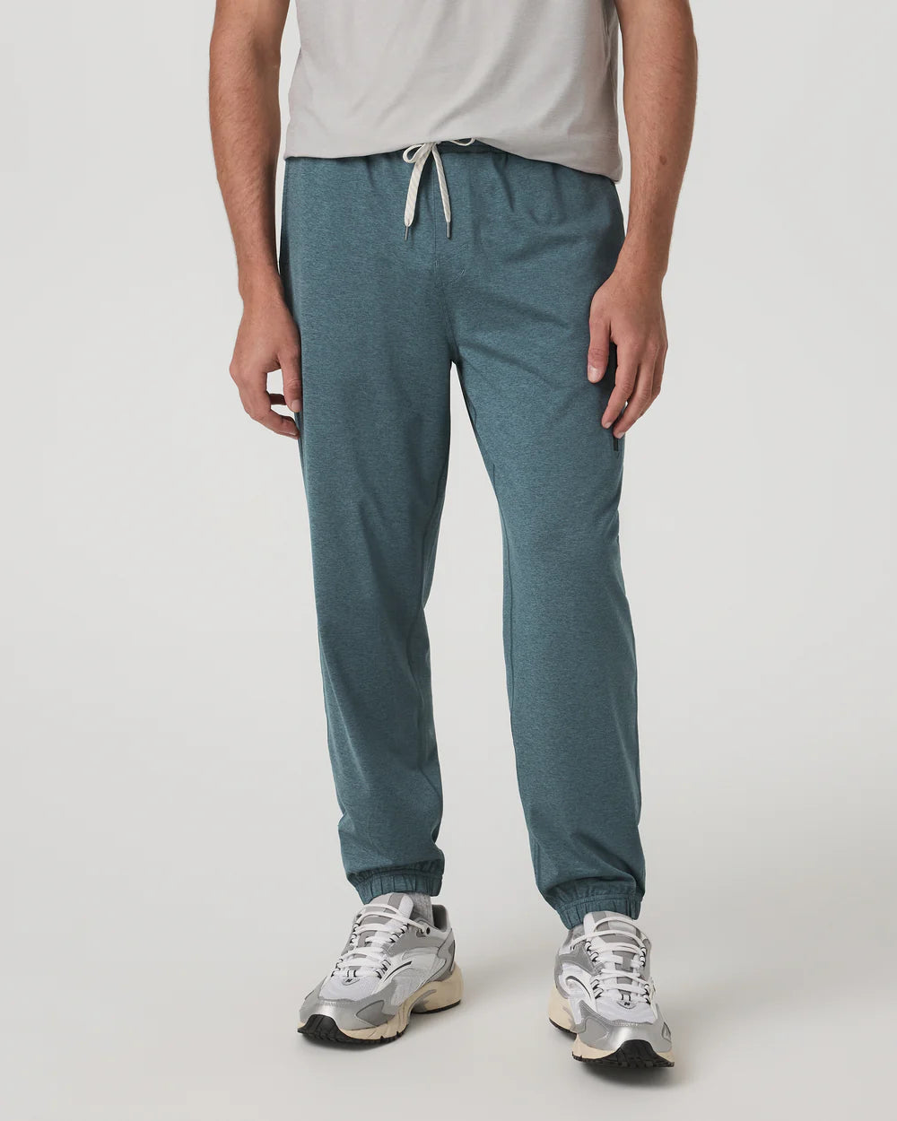 Person wearing teal jogger pants and white sneakers on a light gray background