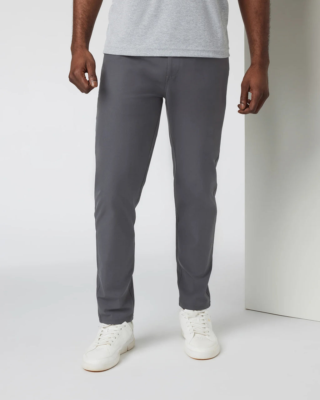 Person wearing gray pants and white shoes on a plain background