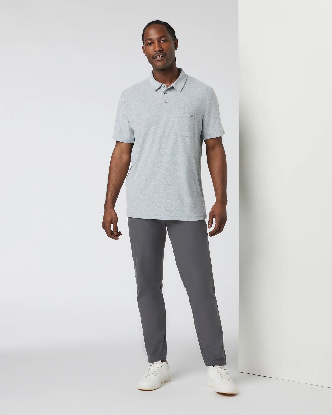 Man wearing a light gray polo shirt and gray pants against a white background