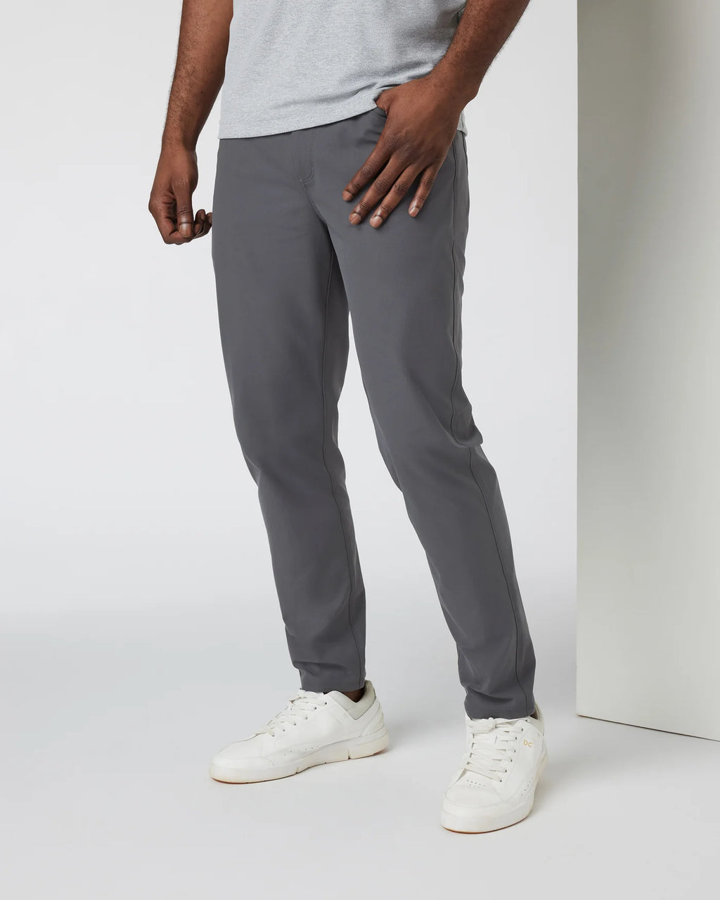 Person wearing gray pants and white sneakers on a plain background