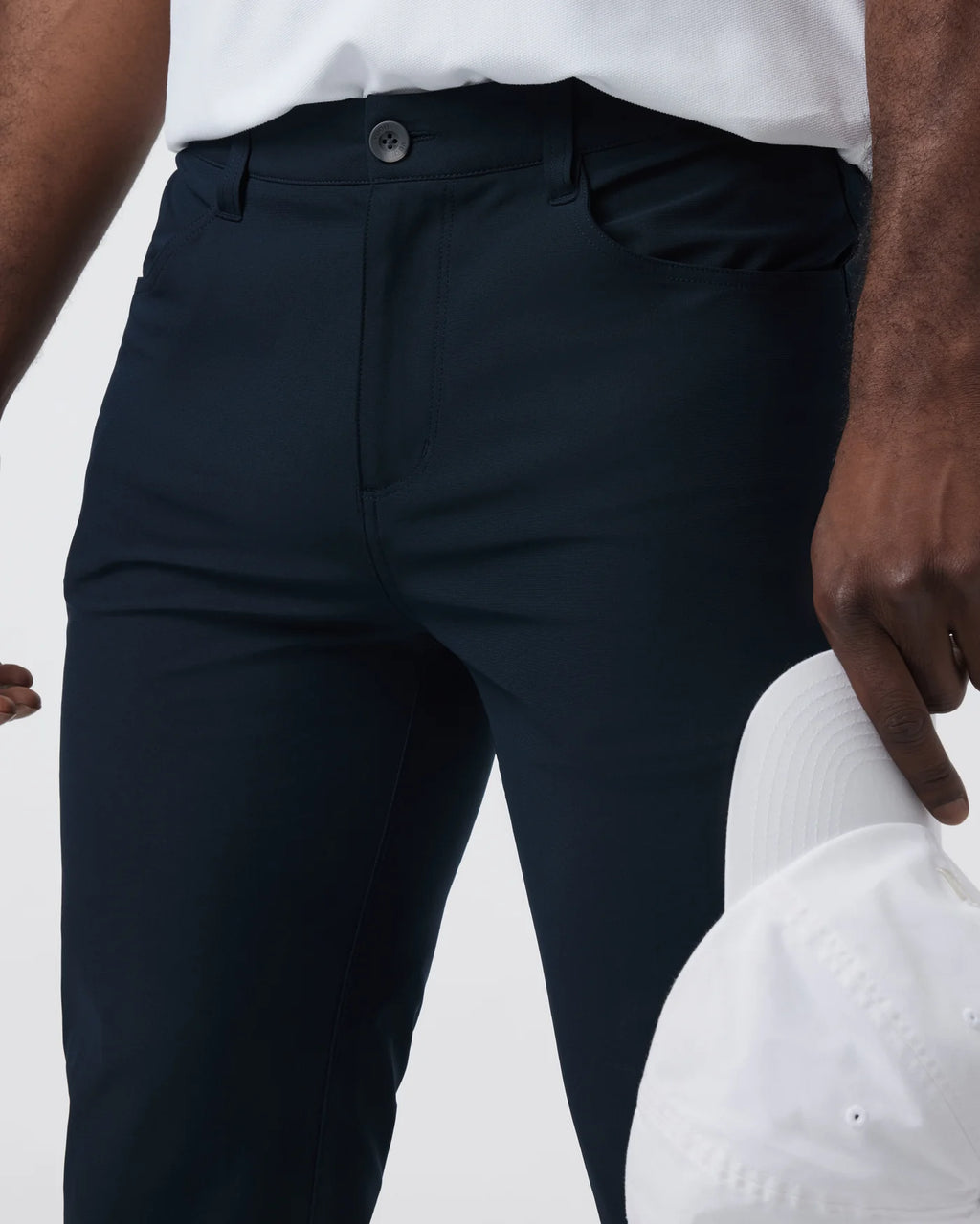 Person wearing navy pants with a white shirt and cap on a light background