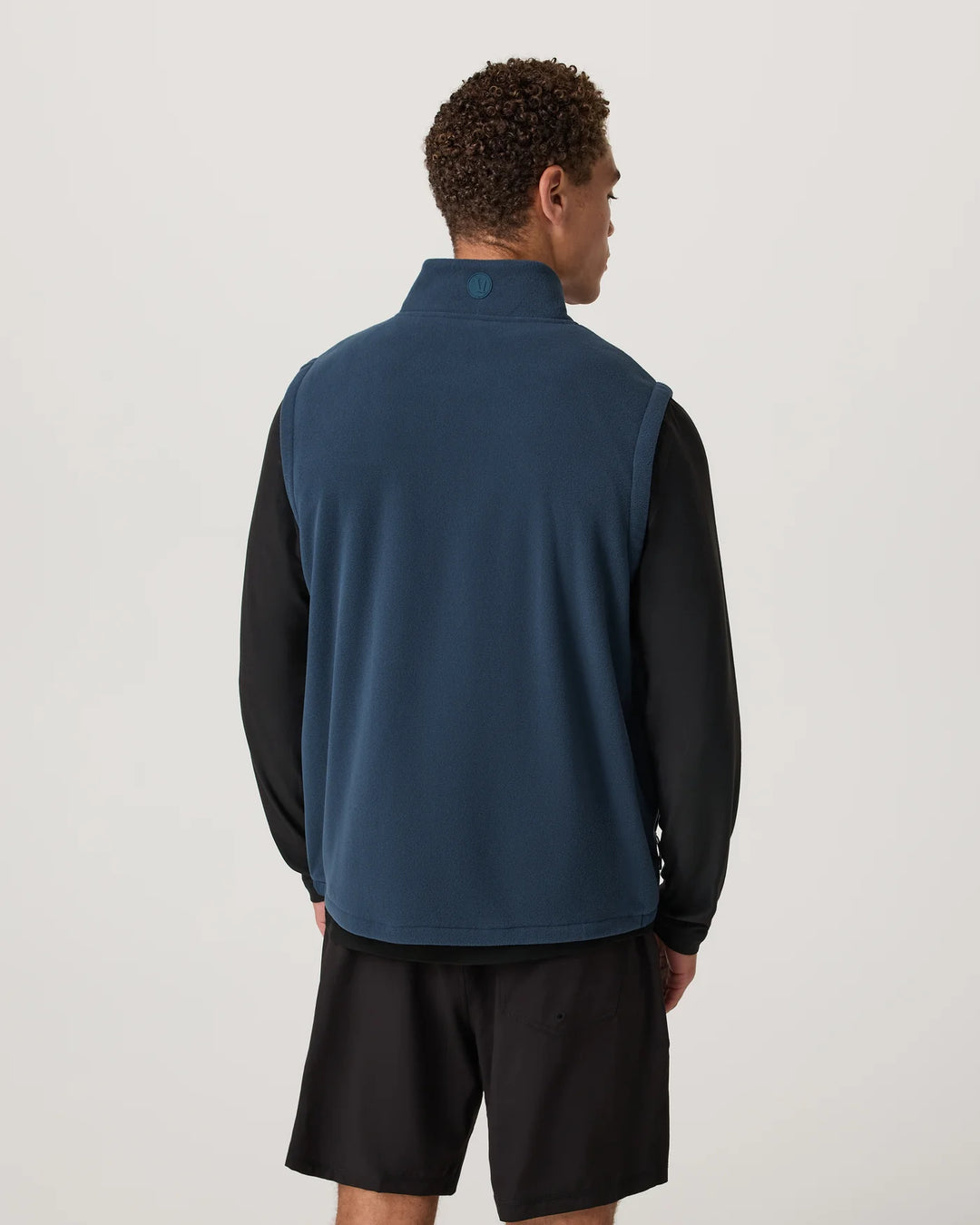 Person wearing a blue vest over a black shirt and shorts on a light gray background