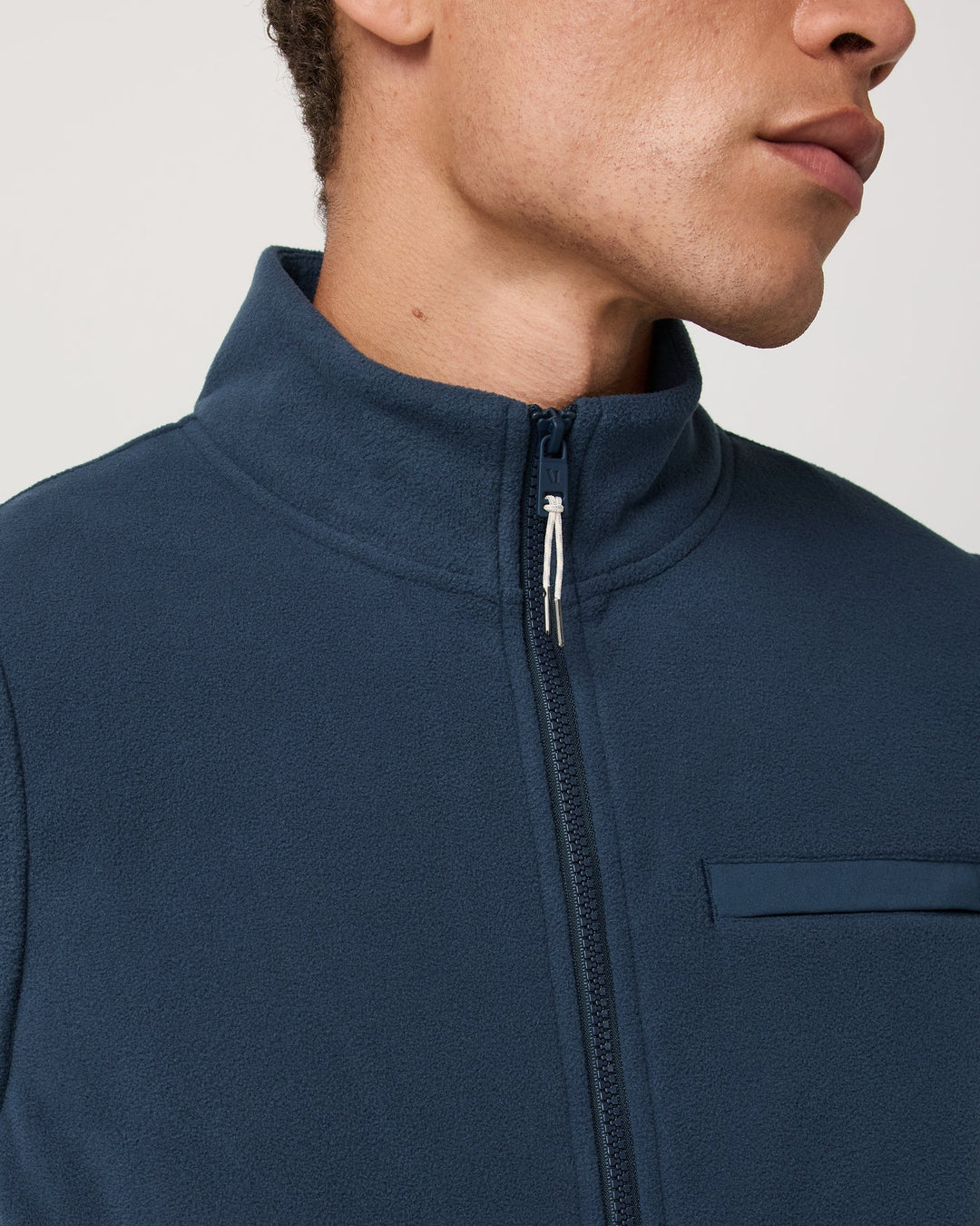 Close-up of a person wearing a blue jacket with a zipper on a plain background