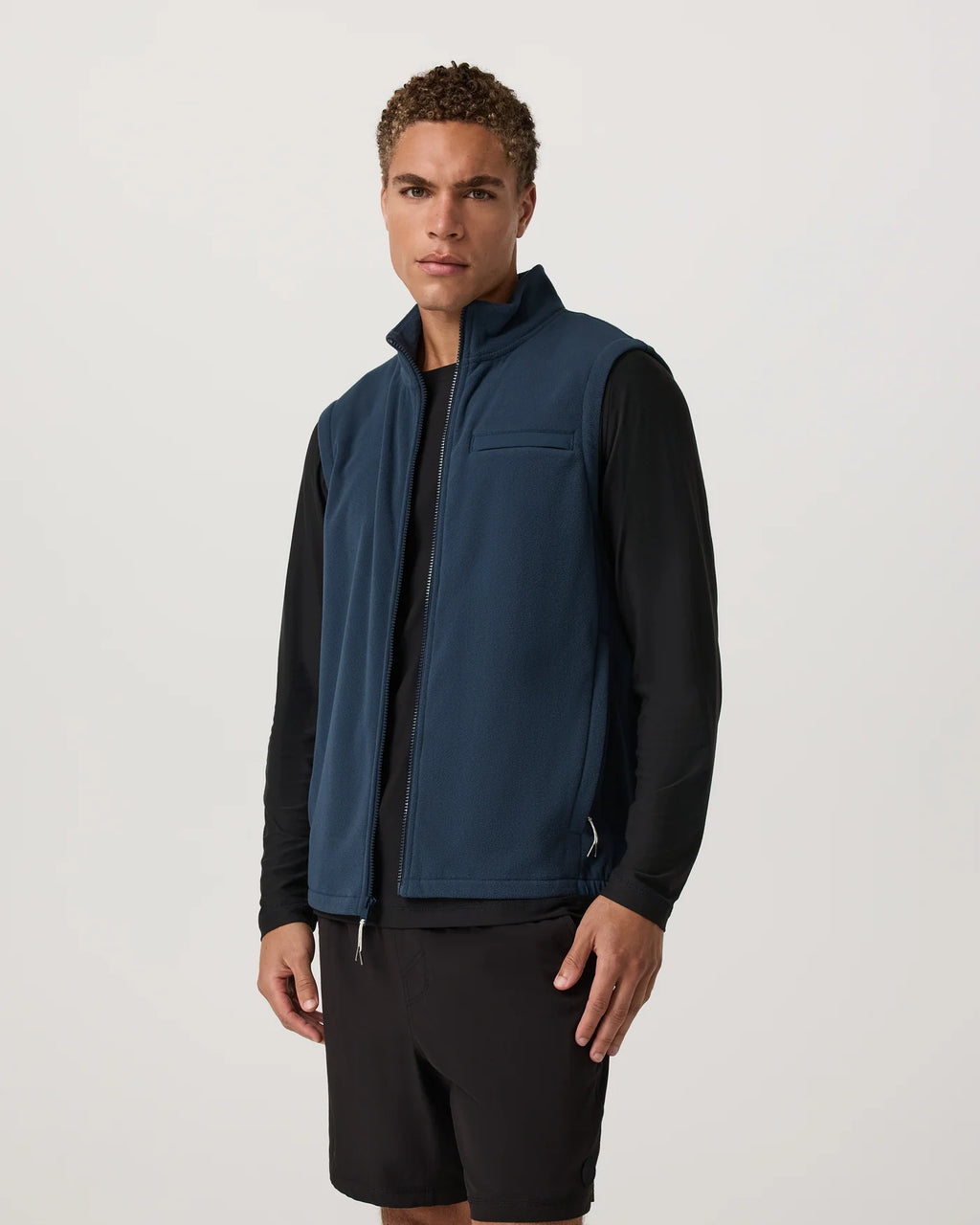 Man wearing a blue vest over a black shirt on a light gray background