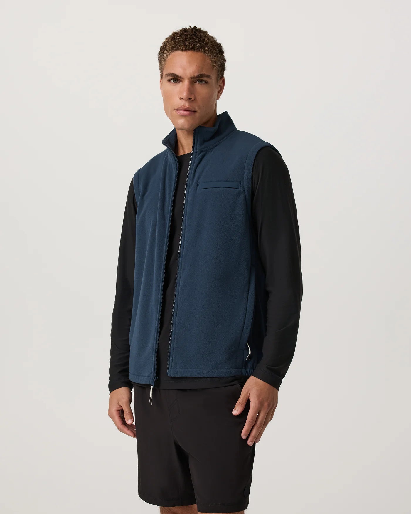 Man wearing a blue vest over a black shirt on a light gray background