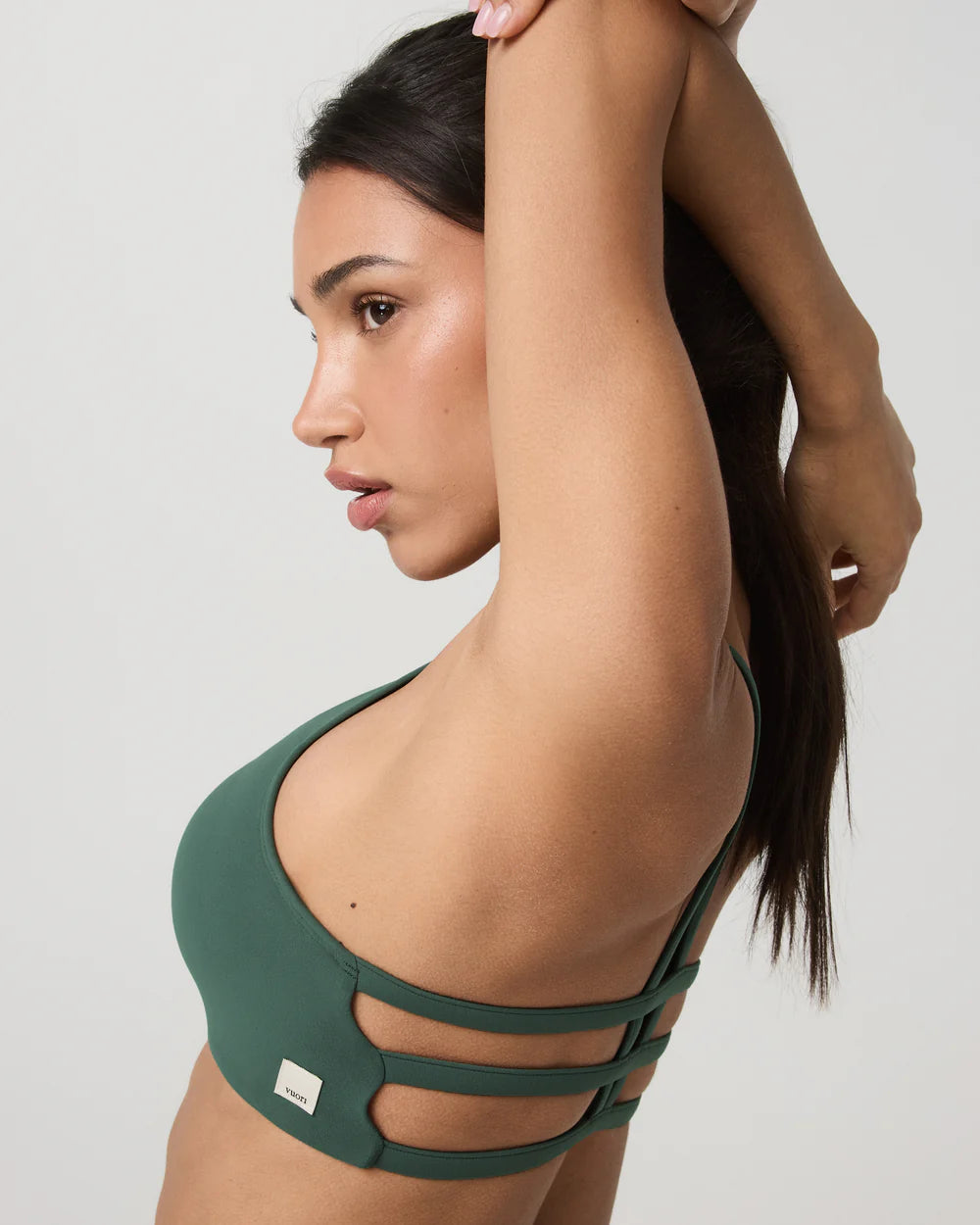 Woman wearing a green sports bra with cut-out design on a plain background