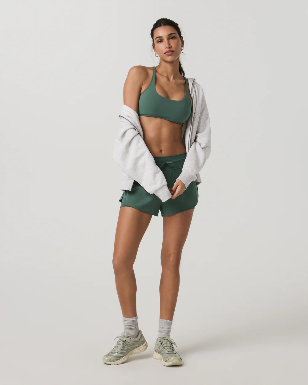 Woman in green athletic wear with a white jacket on a light gray background