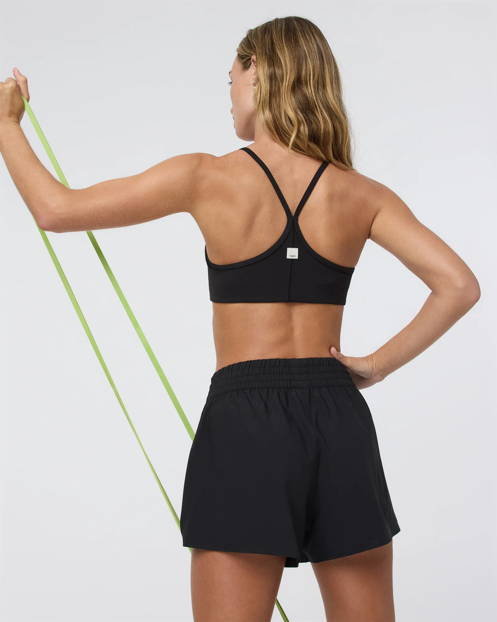 Woman in black sports bra and shorts holding a resistance band against a white background