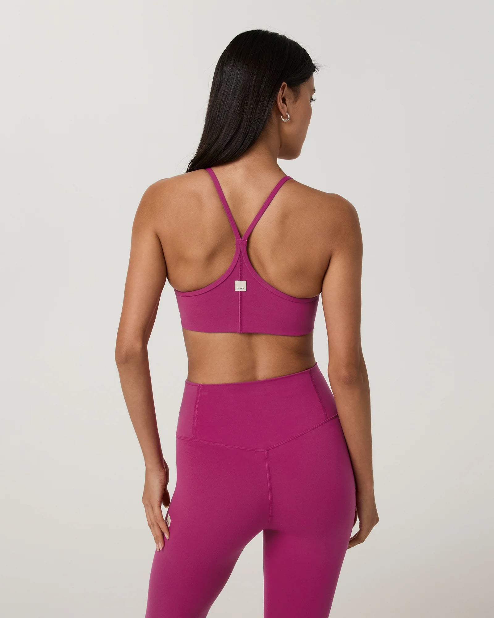 A woman shown from the back wearing a bright magenta sports bra and matching high-waisted leggings against a light gray studio background.